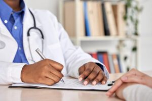 A healthcare professional sits across from a patient and takes notes during a physical