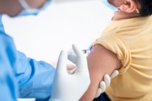A doctor wearing gloves and a mask injects a vaccine into a patient's arm