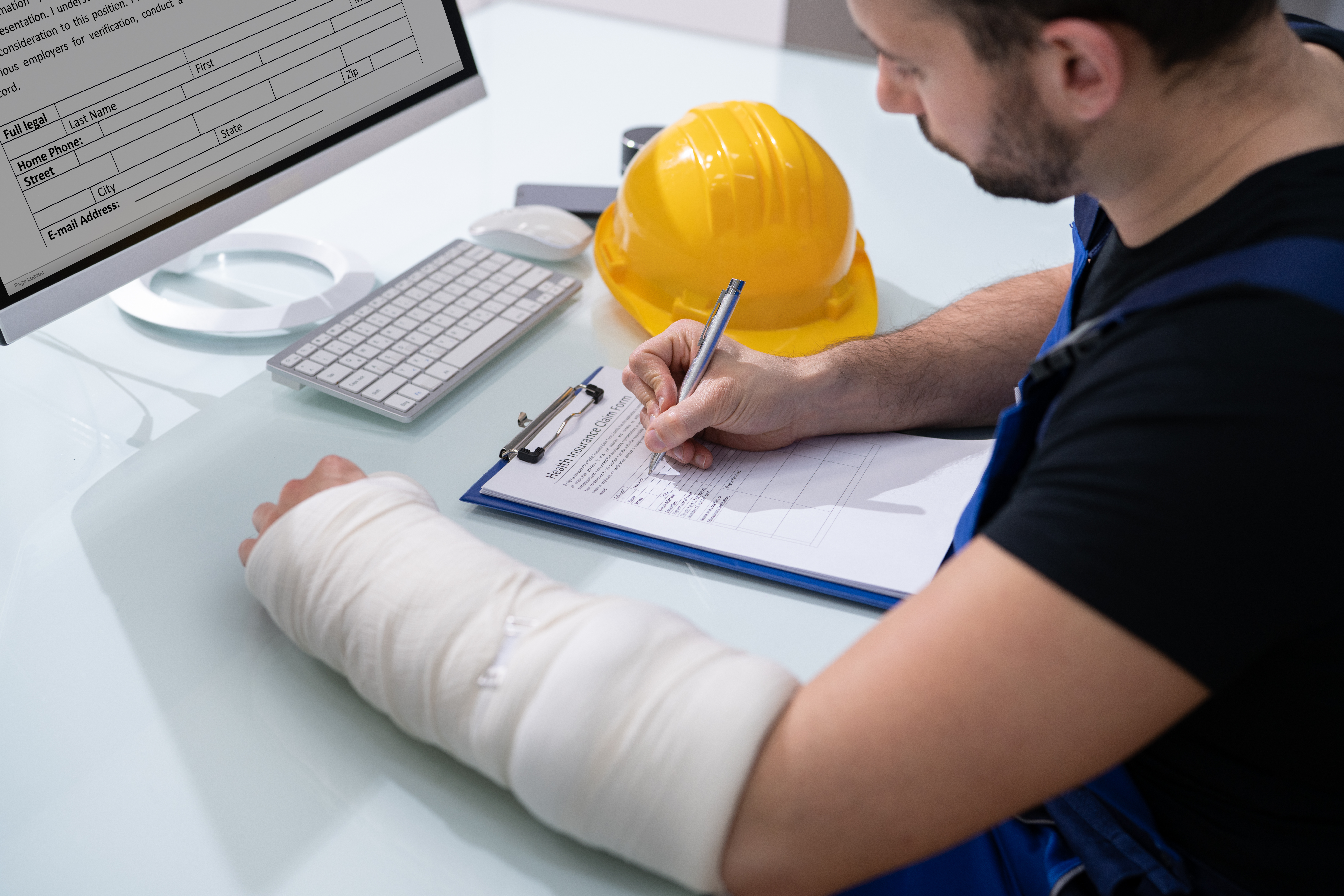 A worker with a yellow hard hat fills out medical informatino form with a cast around his arm