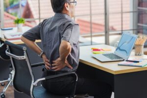 An office worker clenches his back in pain white seated at his desk