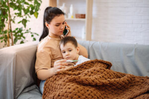A sad sick boy is lying on the couch, feels a fever, has a cold, flu. The worried mother presses the phone to her ear and calls the family therapist after measuring the childs temperature