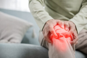 A man grips his knee which is glowing red to signify pain