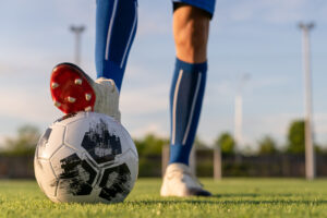 Close-up of athlete standing on soccer ball on field
